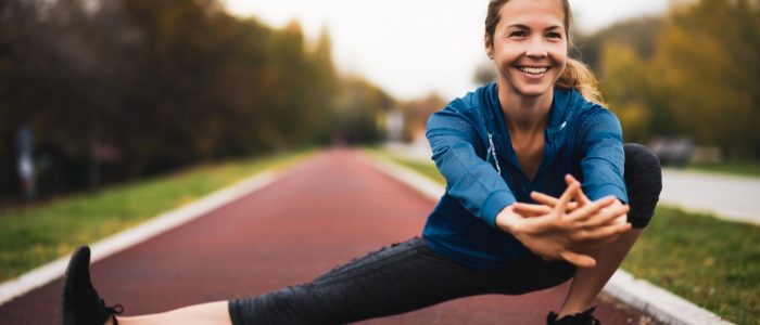 Athlete stretching and smiling beside an outdoor running track